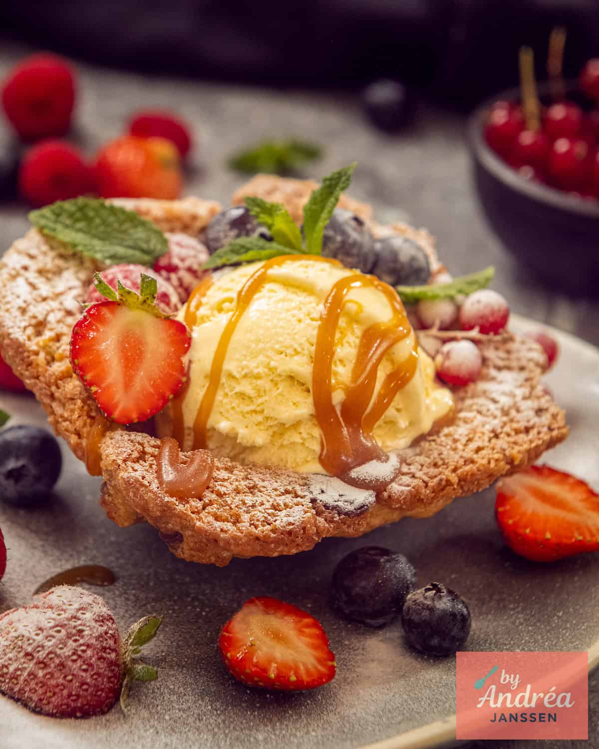 Een koekbakje met een bolletje ijs, vruchten en karamelsaus.