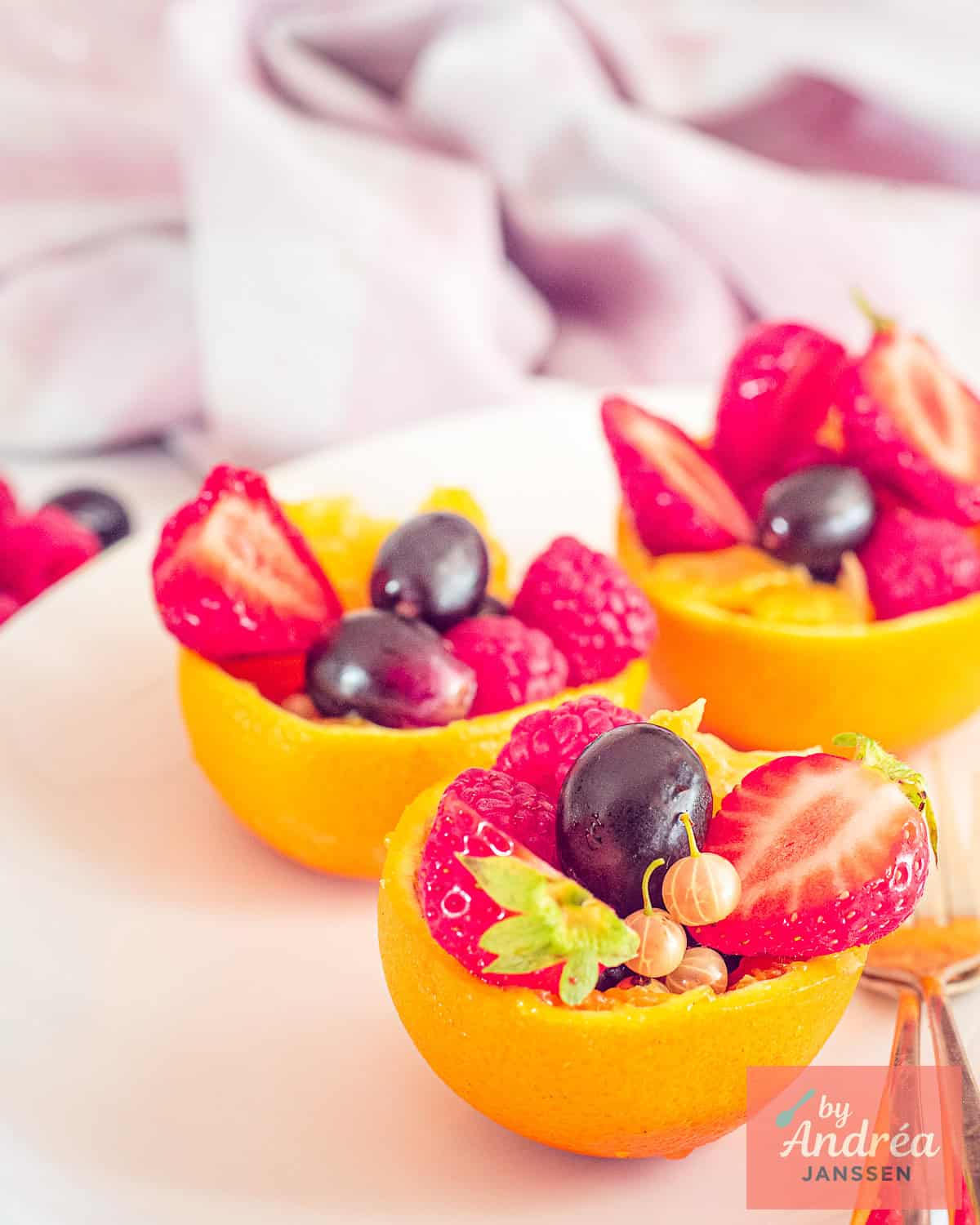 Three orange cups with strawberries, grapes, melon and other fruit