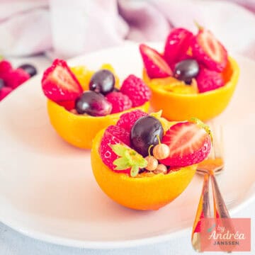 A square picture with three orange bowls filled with fresh fruits on a white plate.