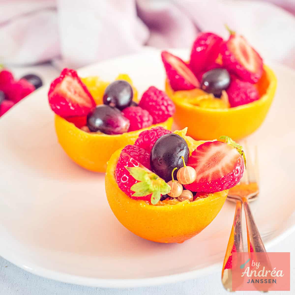 A square picture with three orange bowls filled with fresh fruits on a white plate.