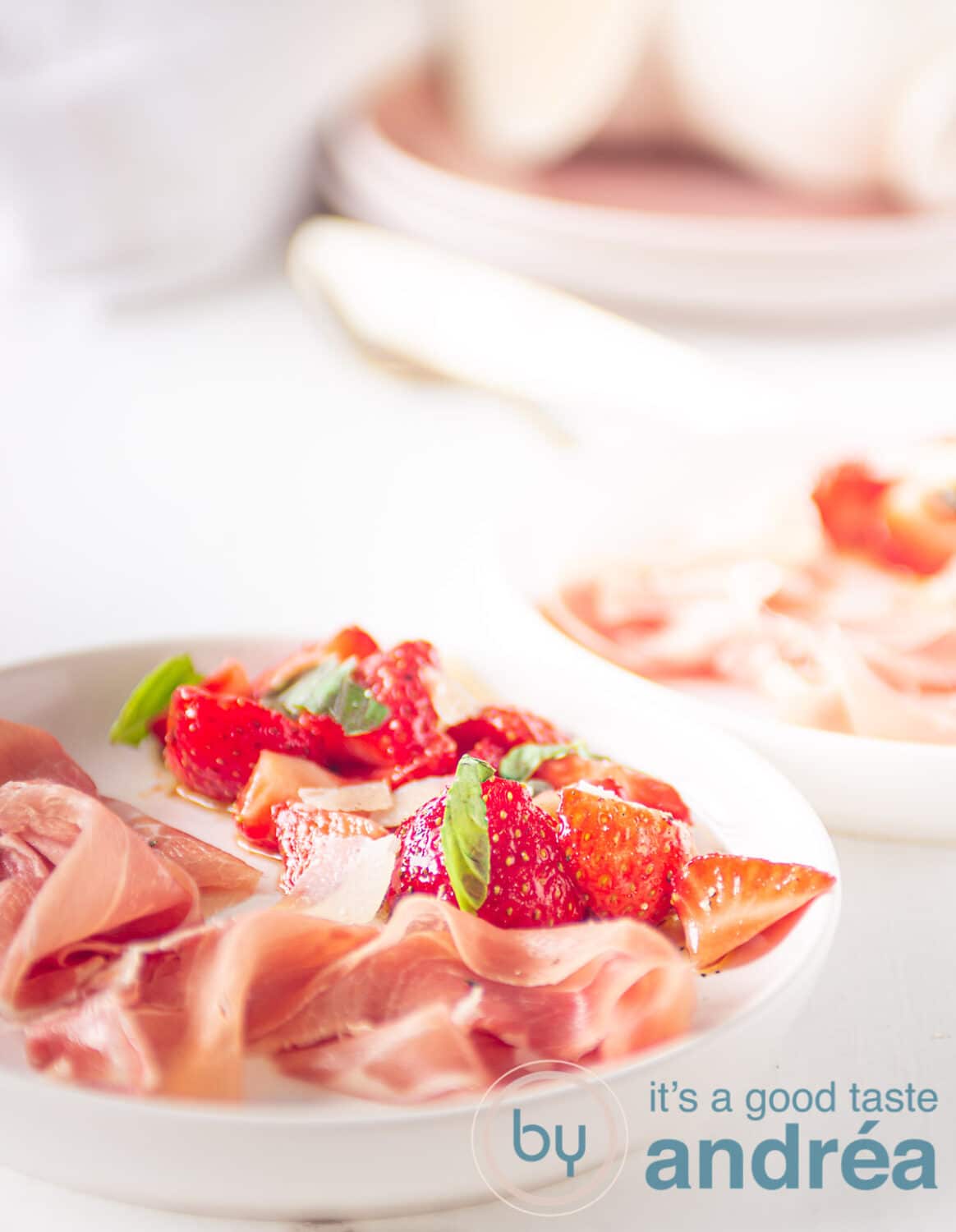 Marinated strawberries and Parmaham on a white plate with plates in the background