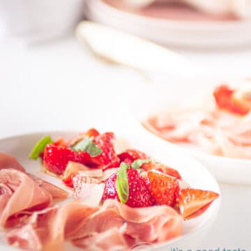 Marinated strawberries and Parmaham on a white plate with plates in the background