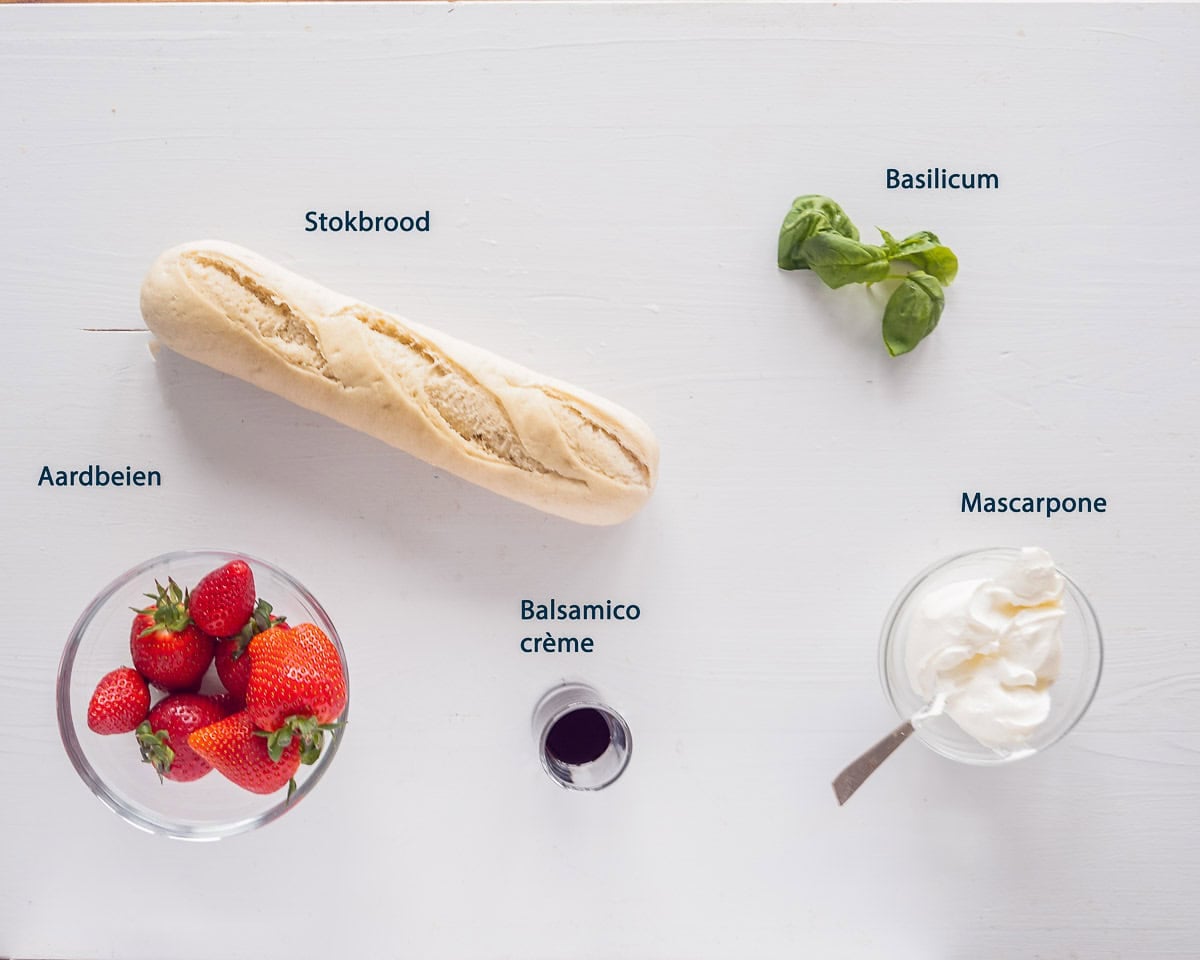 Ingredienten Bruschetta met aardbeien en mascarpone op een witte ondergrond met tekstbeschrijving