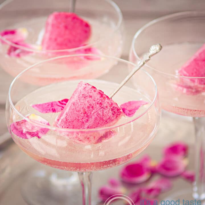 3 champagne glasses with champagne, rose leaves and raspberry popsicle on a sliver plate