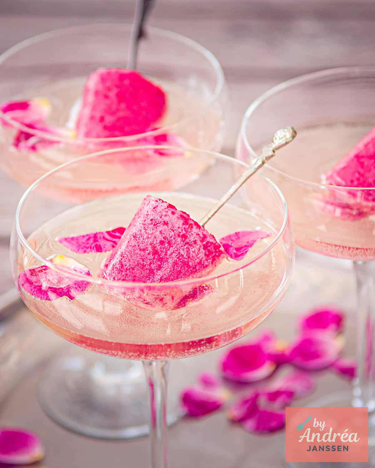 Drie glazen gevuld met champagne en rozenblaadjes en een ijslollie met frambozen.