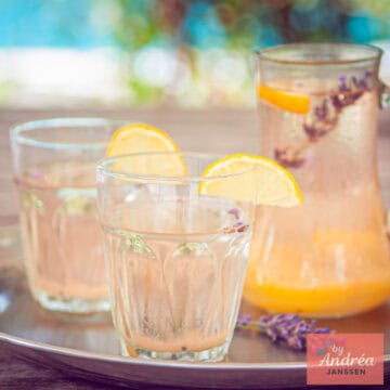 On a silver tray, two glasses and a carafe of lavender lemonade. A square photo.