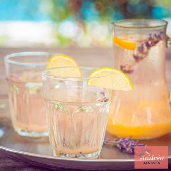 On a silver tray, two glasses and a carafe of lavender lemonade. A square photo.