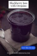 A jar of blackberry jam with oregano on a jute sheet against a dark background. A caption reads: Blackberry Jam with Oregano
