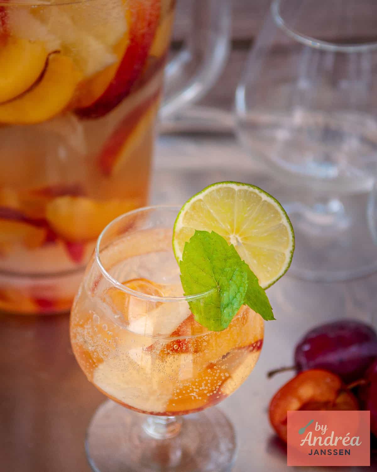 A glass filled with Sangria Bianco with summer fruit, a glass pitcher with more sangria
