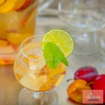 A square photo with a glass of sangria with cava and summer fruit. A pitcher behind it.