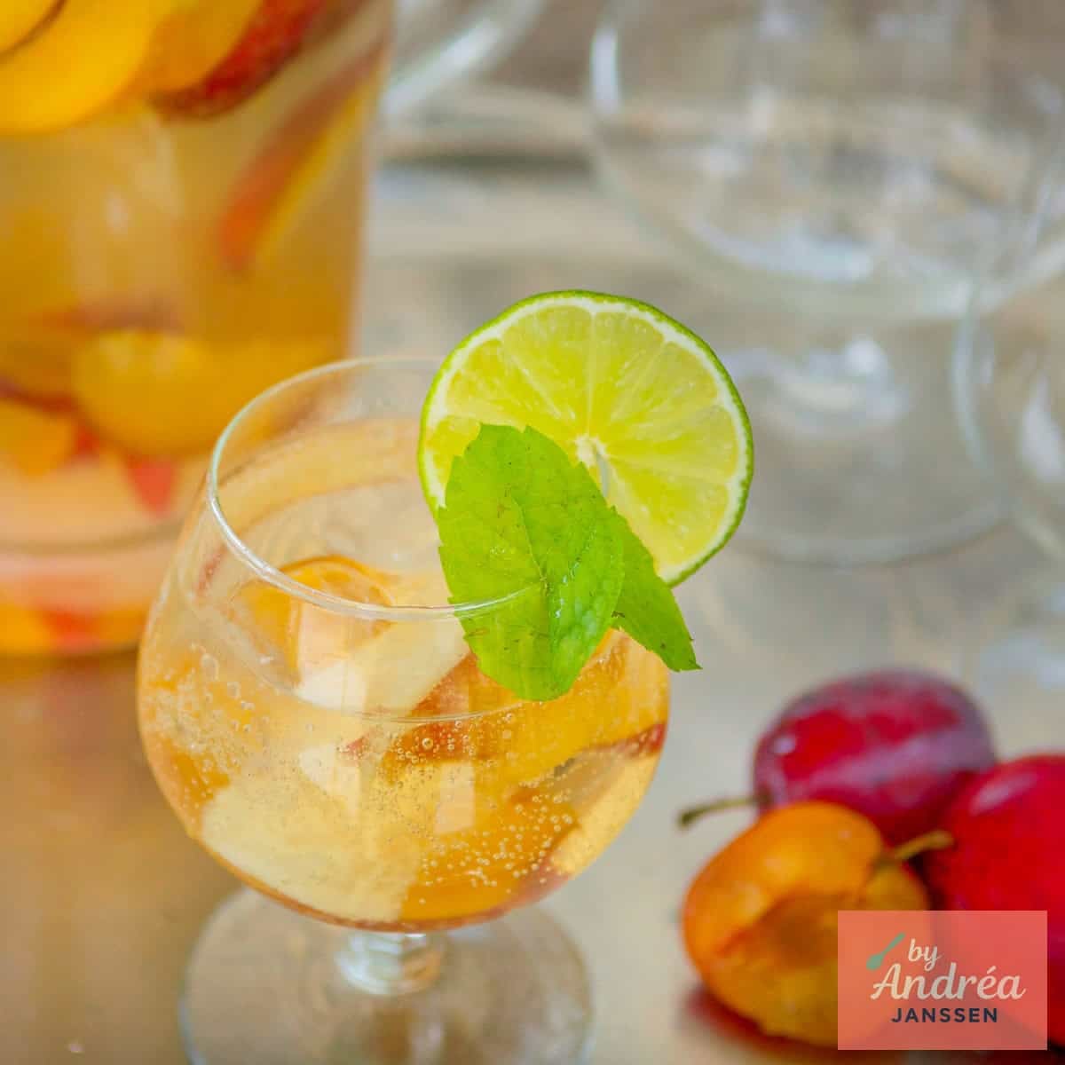 A square photo with a glass of sangria with cava and summer fruit. A pitcher behind it.