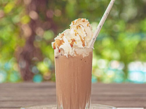 A square photo of a frappuccino on a wooden table.