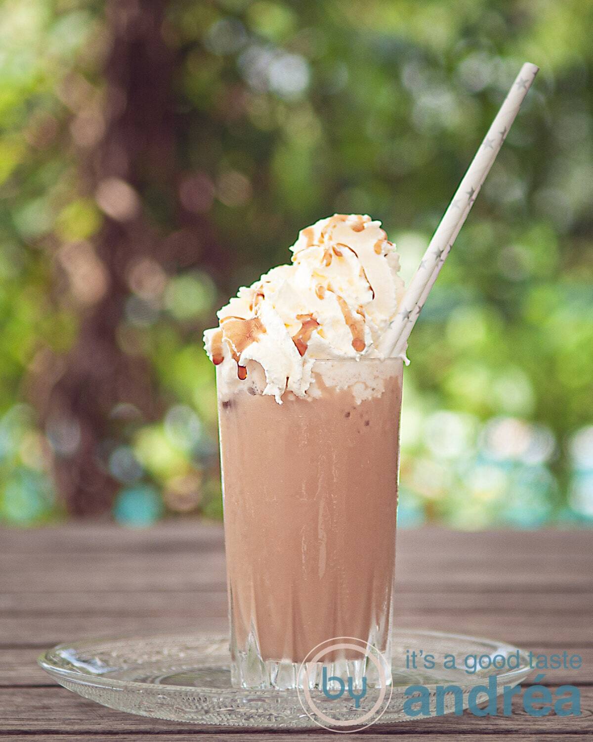 Easy Homemade Starbucks Caramel Frappuccino 2 A Frappuccino with whipped cream and caramel sauce on a wooden table, with a green background