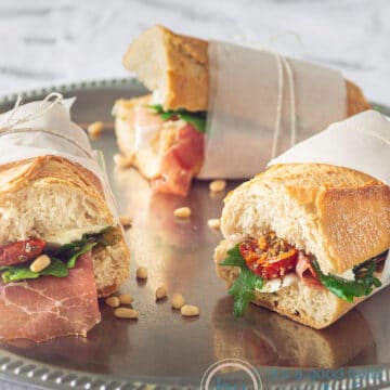Three Italian flavored sandwiches with parma ham, arugula, sun dried tomatoes and Mozzarella wrapped on a silver plate