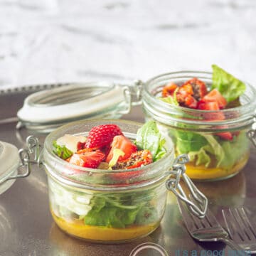 two jars with a green salad, sun-dried tomatoes, strawberries and a honey mustard dressing
