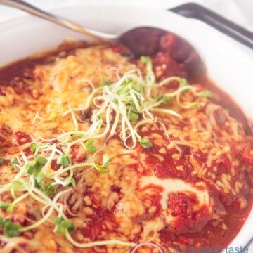 a black casserole dish with schnitzel, lost of vegetables and cheese