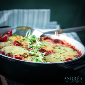a black casserole dish with schnitzel, lost of vegetables and cheese