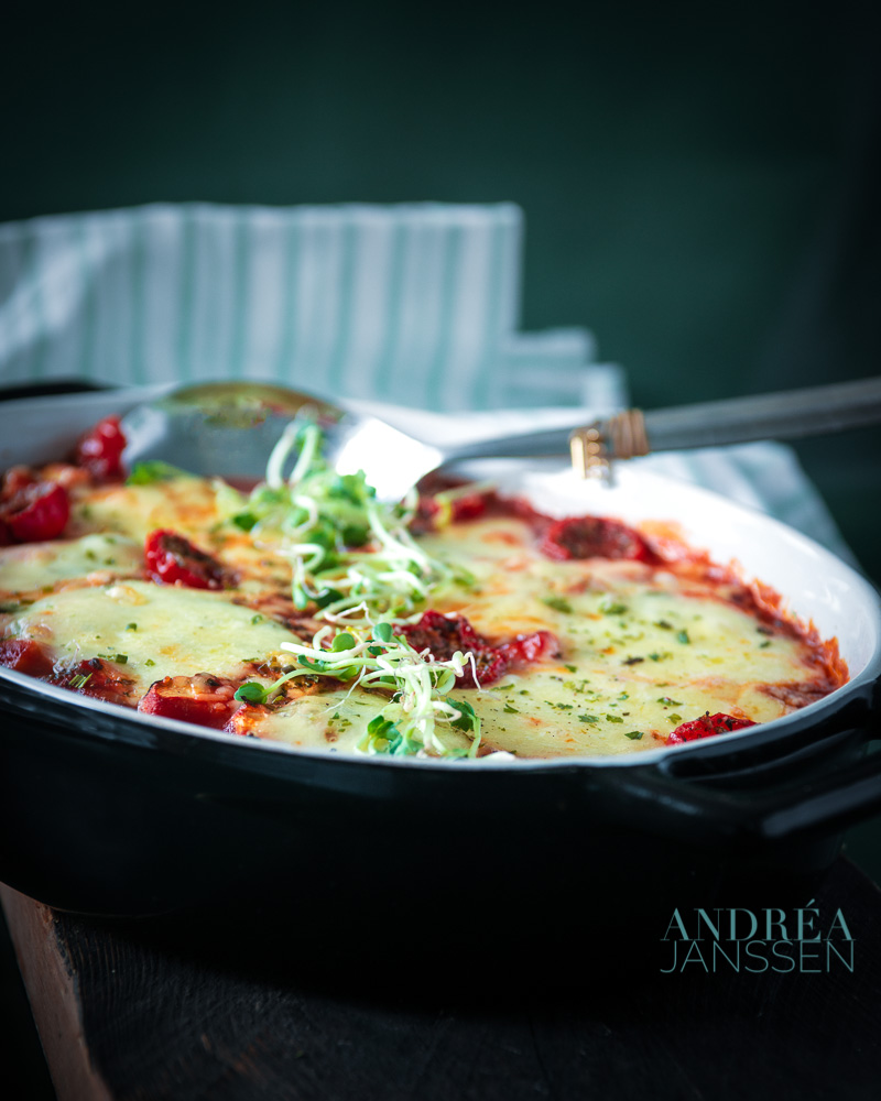 a black casserole dish with schnitzel, lost of vegetables and cheese