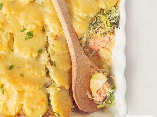 A square photo showing part of a baking dish filled with salmon, leek and potato slices