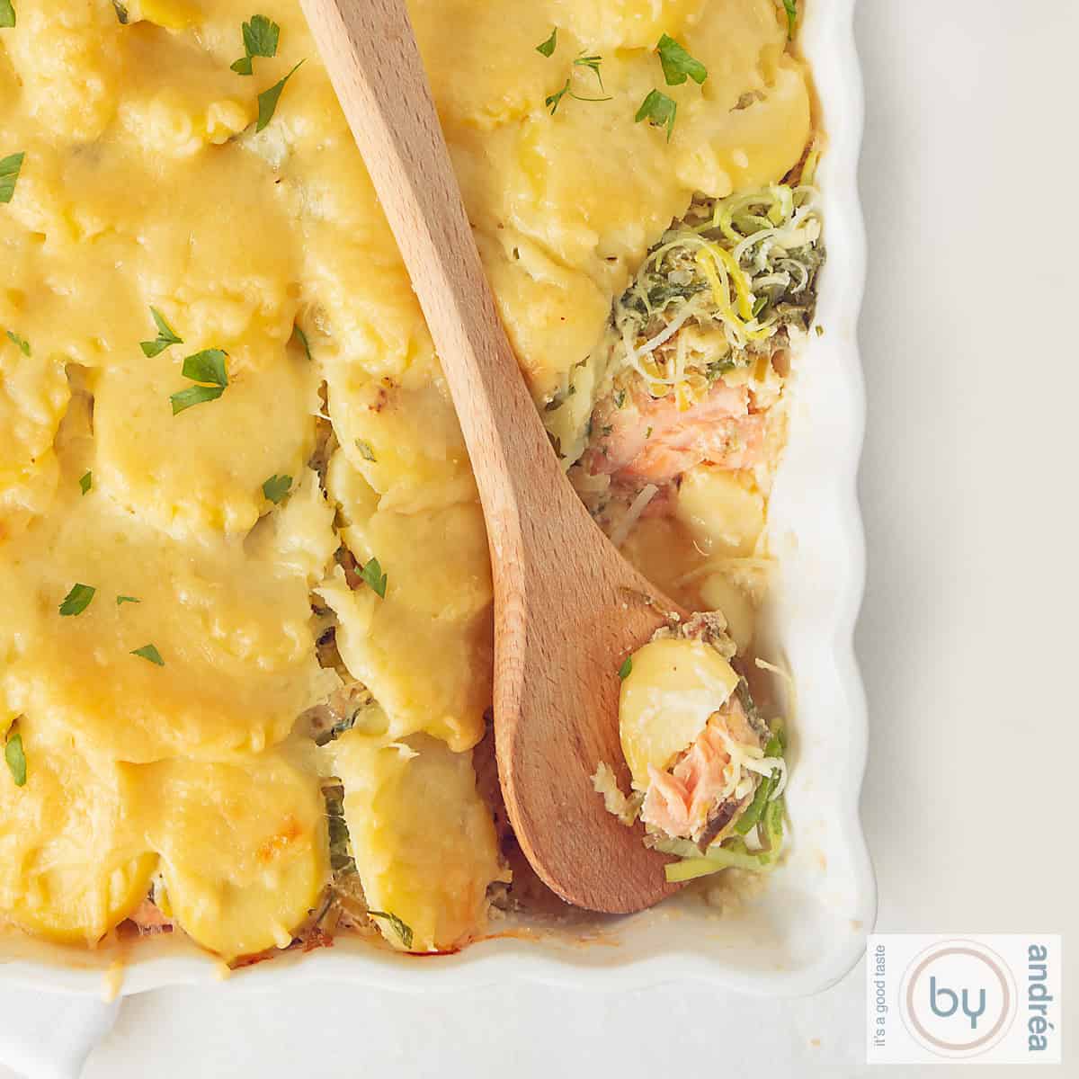 A square photo showing part of a baking dish filled with salmon, leek and potato slices