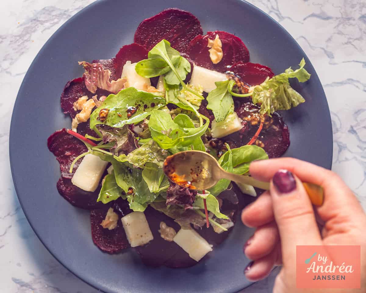 Plakjes bieten met kaas, peer, gemengde sla waarover dressing wordt verdeeld