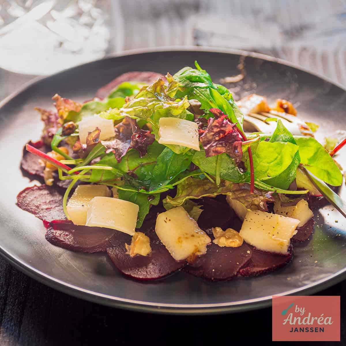 A square photo with a plate of beetroot, pear, cheese, lettuce, and walnut carpaccio.
