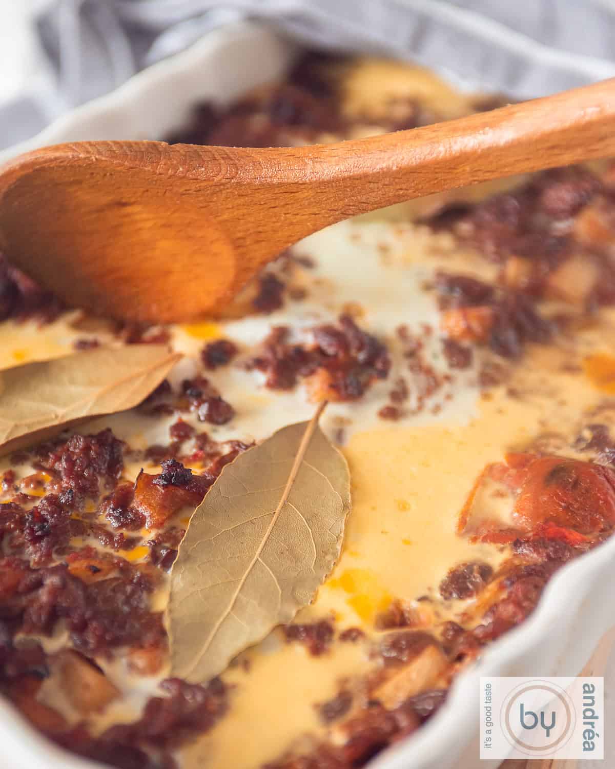 A portion of a white baking dish with an egg layer, minced meat, bay leaf, apple and raisins: African Bobotie