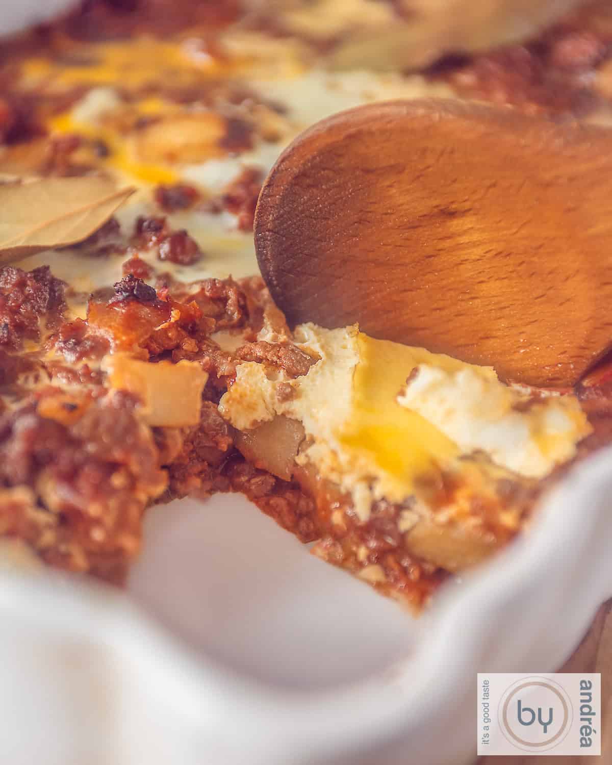A portion of a bobotie casserole dish with a scoop removed. A wooden spoon is stuck inside.