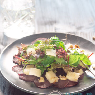 a white plate with beet carpaccio, pear, arugula, old cheese and walnuts