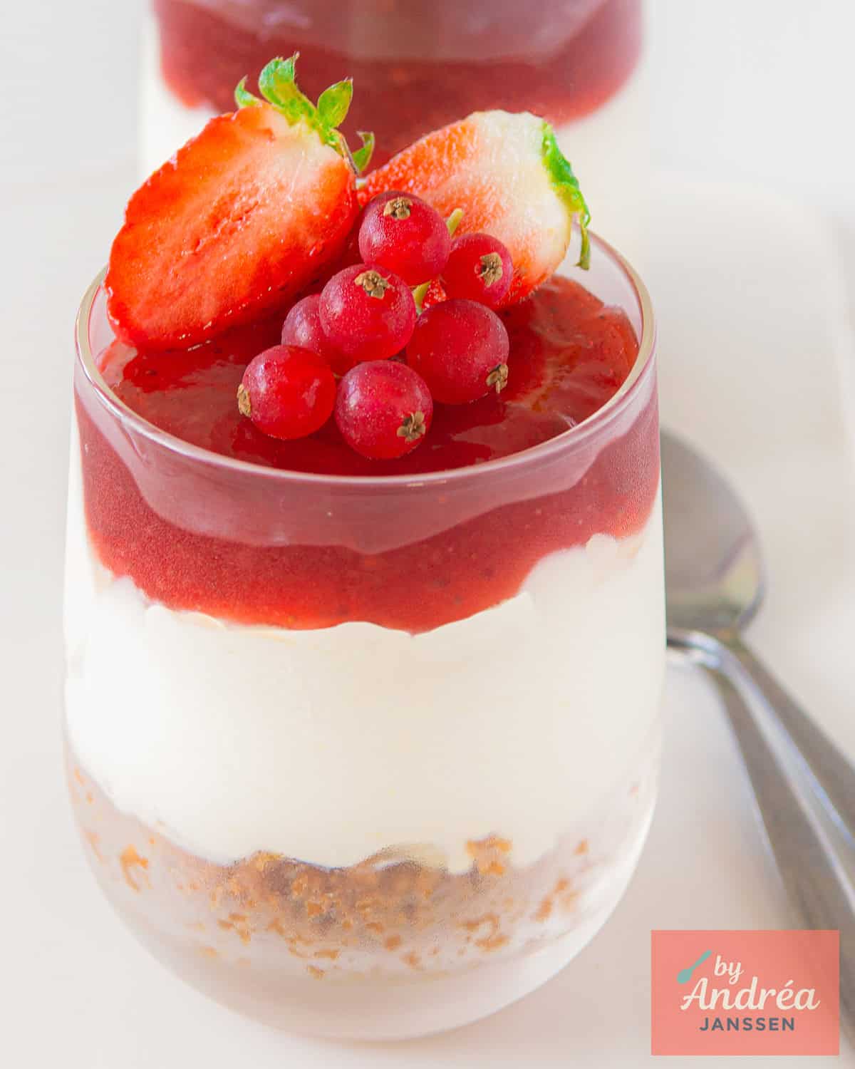 A glass with no bake cheesecake with red fruit on a white background