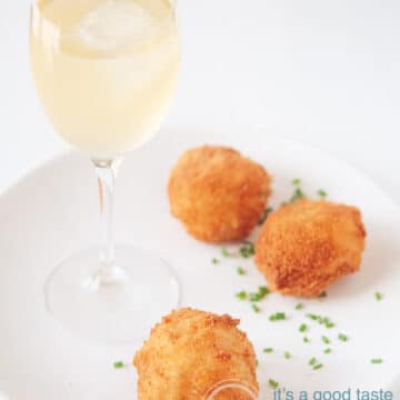 Three shrimp bitterballen on a white plate, sprinkled with chives. A glass of white wine to accompany the dish