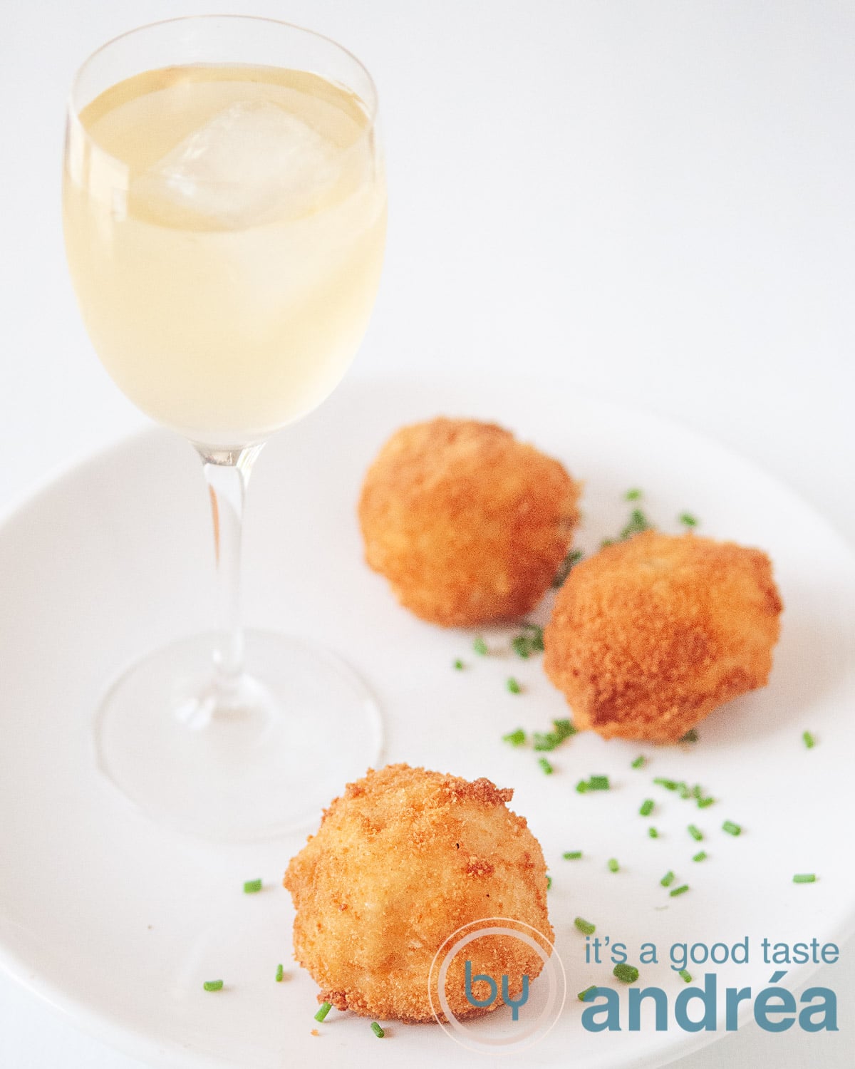 Three shrimp bitterballen on a white plate, sprinkled with chives. A glass of white wine to accompany the dish