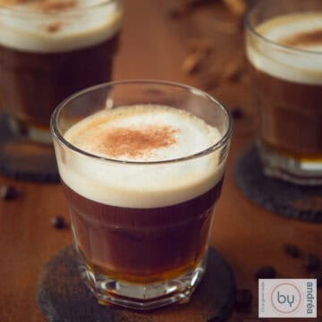 A square photo with a brown table with three cups of apfelcorn honey cafe au lait poured into it.