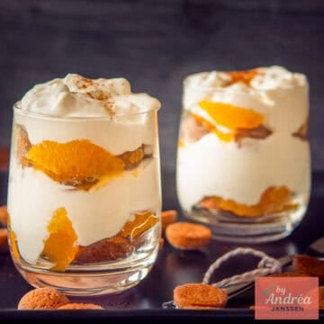 A square photo with two glasses of pepernoten mandarin tiramisu diagonally behind each other on a black background.