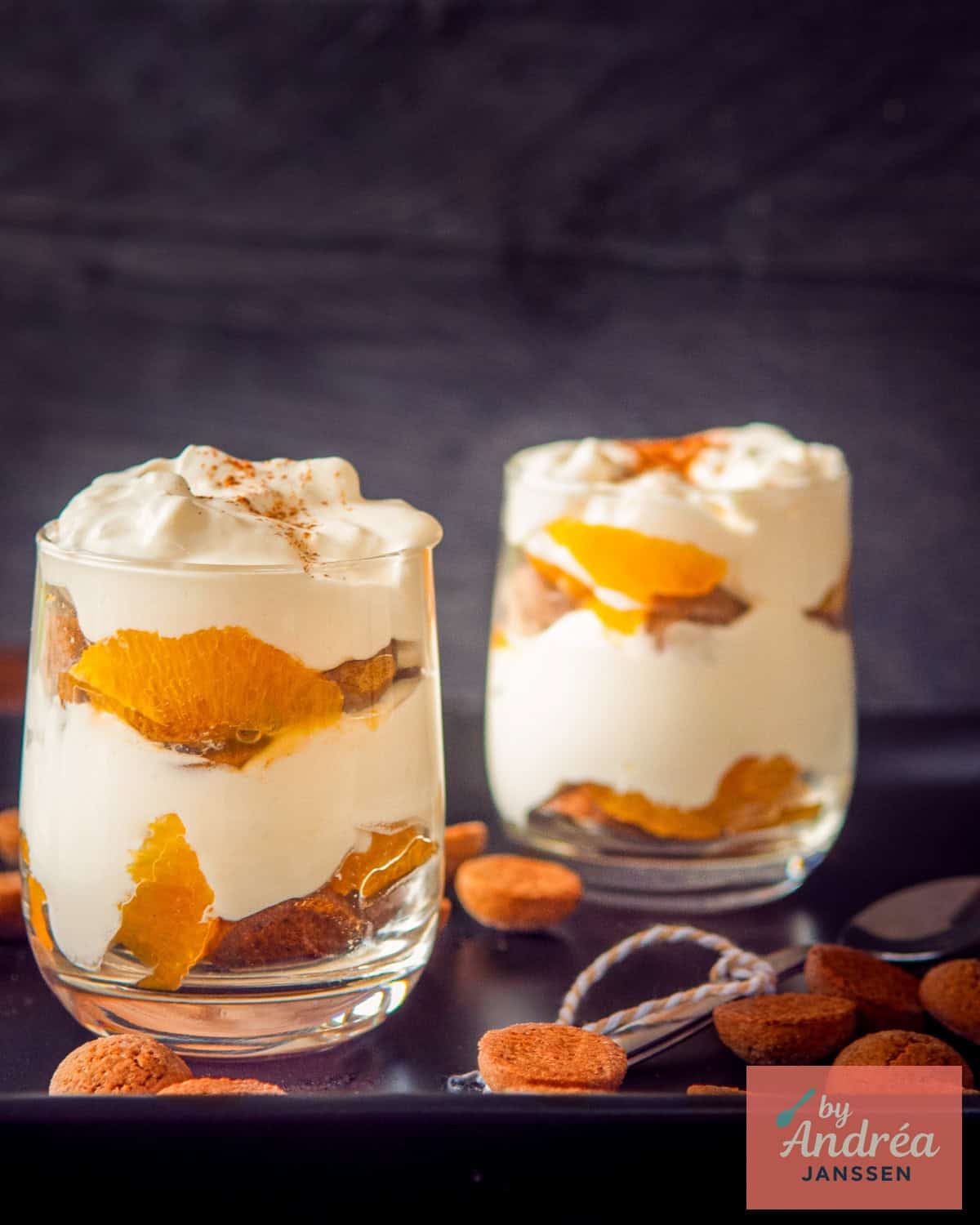 Een zwart bord met pepernoten daarop twee glaasjes gevuld met pepernoten tiramisu met mandarijn.