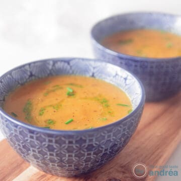 A square photo with two blue bowls filled with pumpkin soup with a delicious herbal dressing.