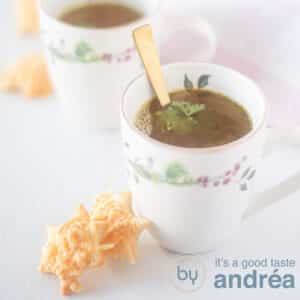 A square photo with a white background, two cups diagonally behind each other. In it a broth. Two cheese stars stand against the first cup.