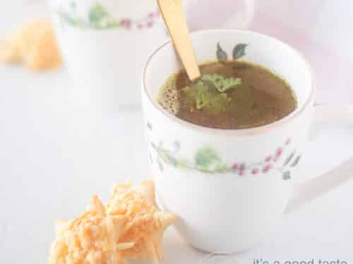 A square photo with a white background, two cups diagonally behind each other. In it a broth. Two cheese stars stand against the first cup.