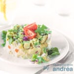 A square photo of a salad of smoked chicken and avocado on a white plate, topped with quartred cherry tomatoes on a white background