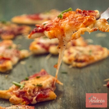 A mini Christmas pizza with melting cheese is lifted on a fork above the other pizzas