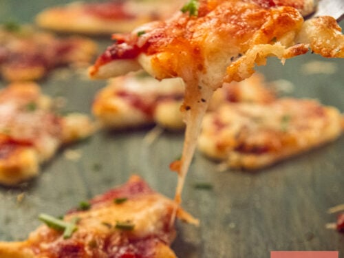 A mini Christmas pizza with melting cheese is lifted on a fork above the other pizzas