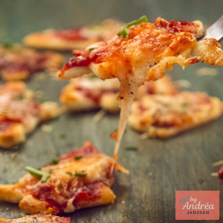 A mini Christmas pizza with melting cheese is lifted on a fork above the other pizzas