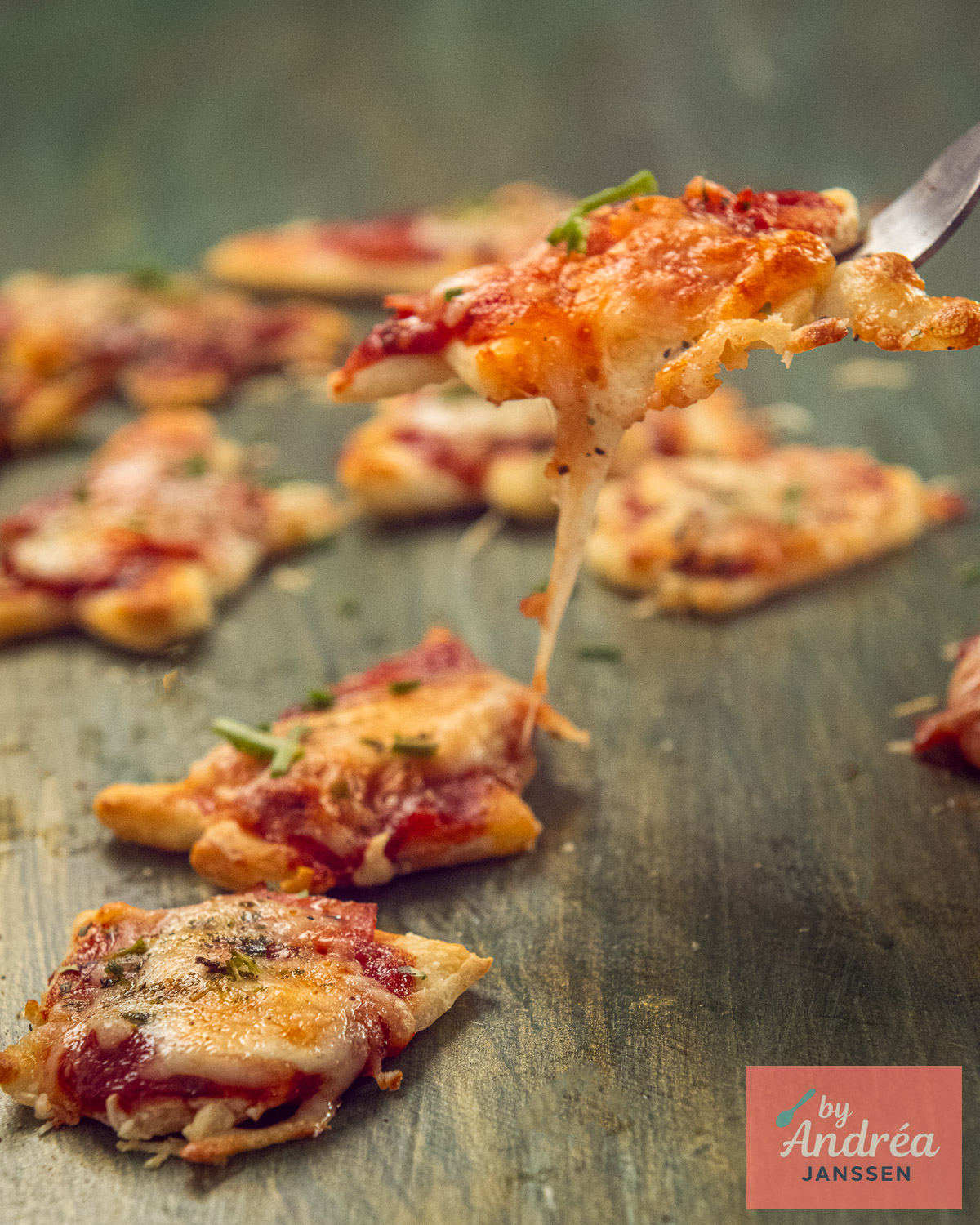 A warm mini Christmas pizza with a long cheese pull is lifted on a fork among the other pizza