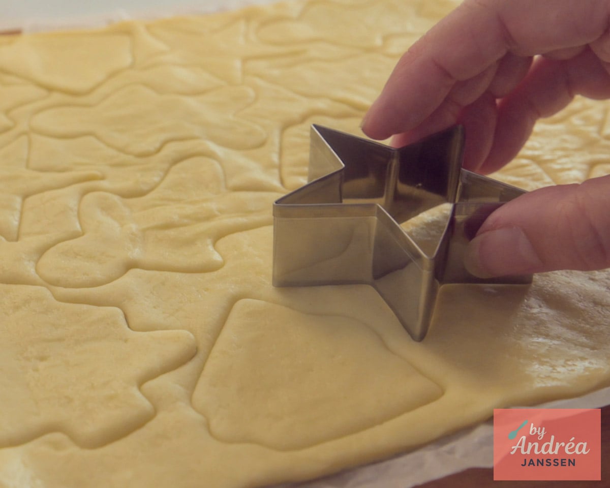 Een hand steekt met een kerstboomvormige uitsteker figuurtjes uit uitgerold pizzadeeg