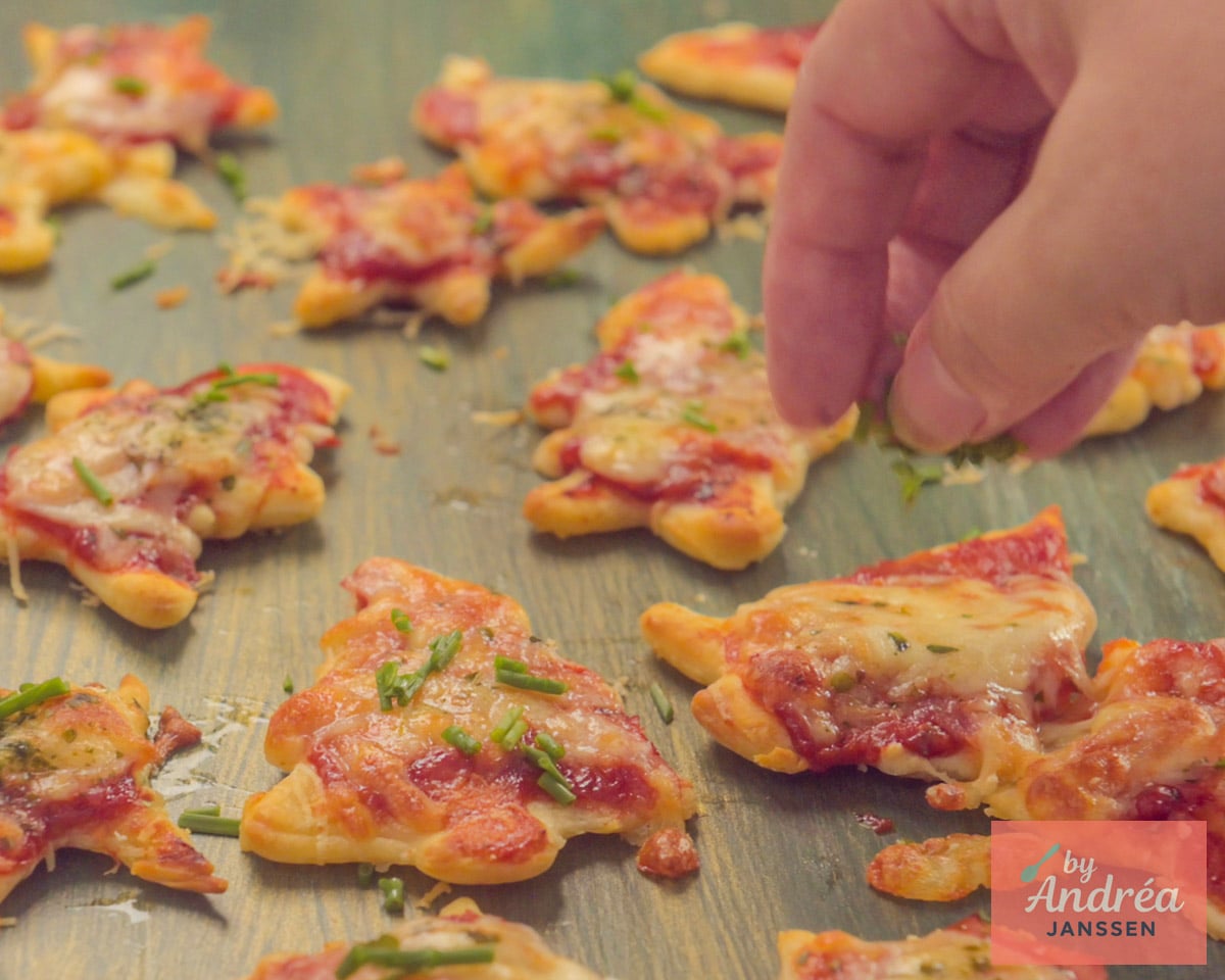 en hand strooit verse fijngesneden bieslook over de gebakken mini kerst pizza's