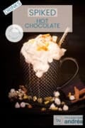 A black mug on a black background with marshmallows, gold stones and cinnamon. A dollop of whipped cream drops down. A text overlay at the top: luxury chocolate milk with licor 43, drinks, easy recipe, hot drink