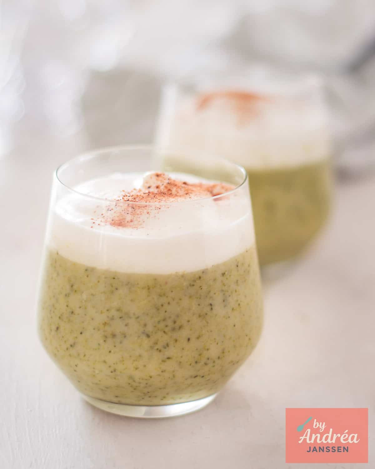 Two glasses of broccoli soup with cream on top.