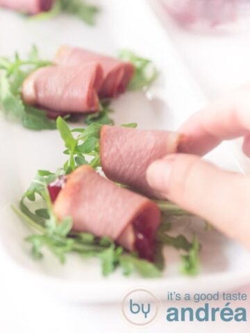 A hand takes a roll of duck breast filled with cranberry compote and arugula
