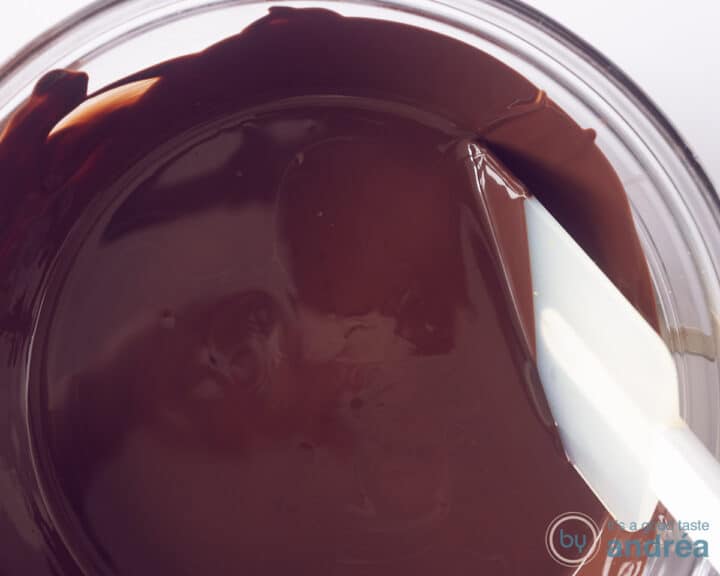 A glass bowl with a white spatula with melted chocolate