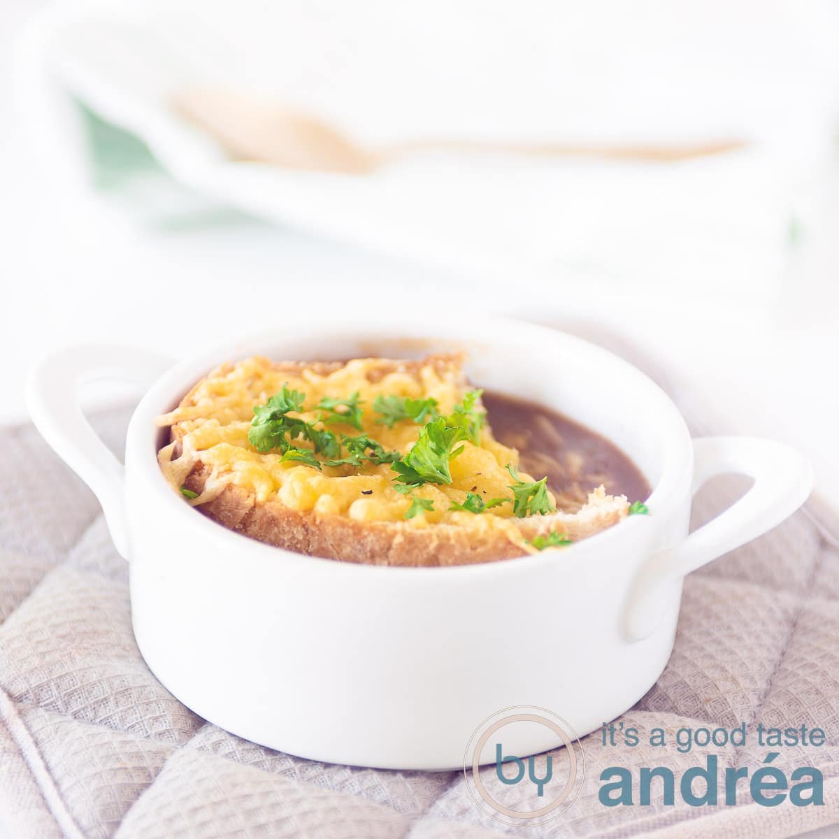 A white soup bowl filled with red onion soup and a piece of gratinated baguette